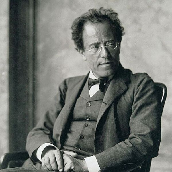 A black-and-white portrait shows a seated person in a suit and bow tie with glasses, turned slightly to the side against a softly textured background.