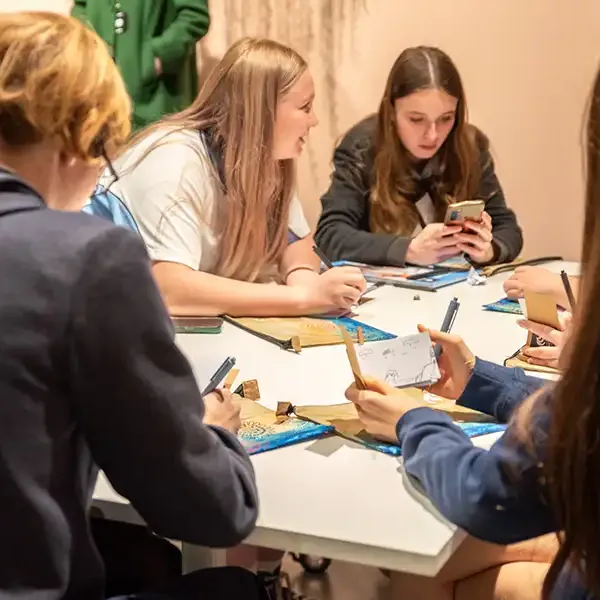 A group of students sit around a table working with pens and paper.