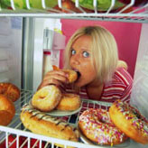 Girl with head in fridge eating donuts