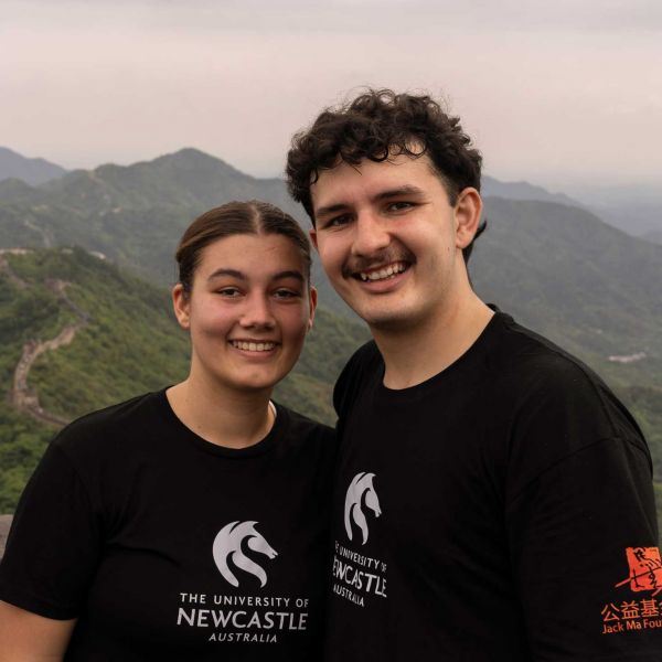 2023 Ma & Morley Scholars, Ryvah and Lauchlyn smiling toward the camera on the Great Wall of China. There are mountains in the background.. Journey of hearts and minds: Ma &.