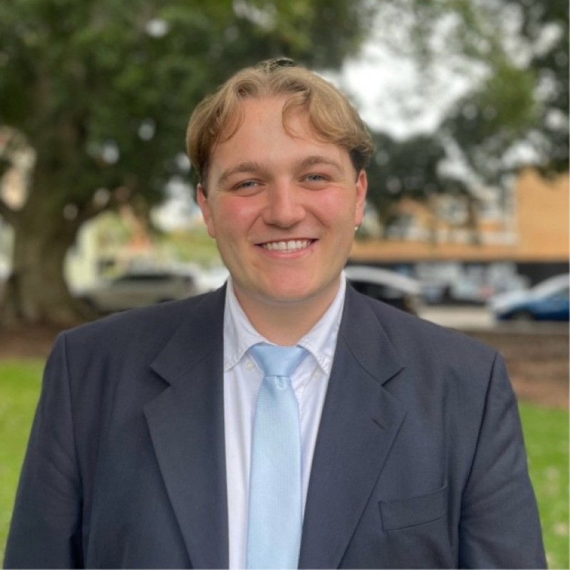 A person smiling at the camera, dressed in suit and tie