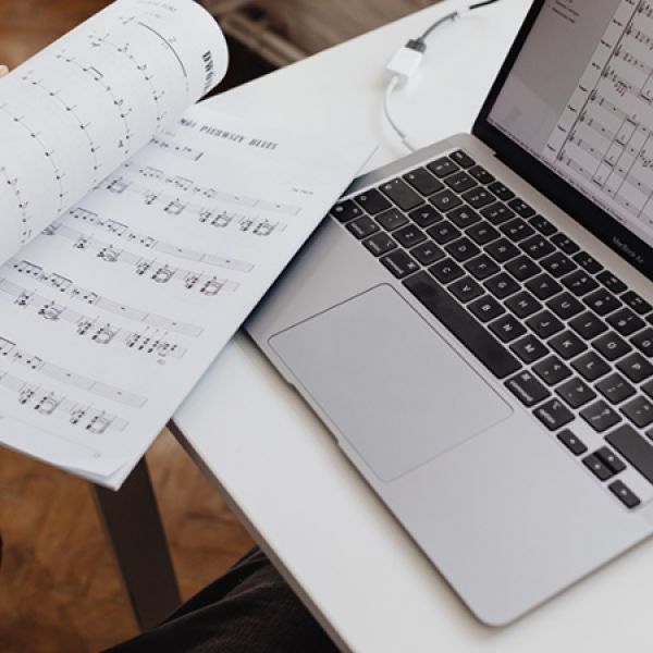 A laptop on a desk displaying sheet music next to printed copies of sheet music.