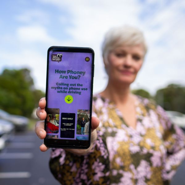 In the foreground is a phone screen with the text 'How Phoney Are you''. Driving down phone use behind the wheel.