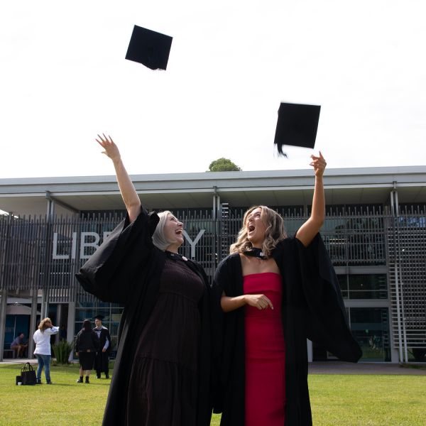 Two graduates throw their caps into the air at Ourimbah campus