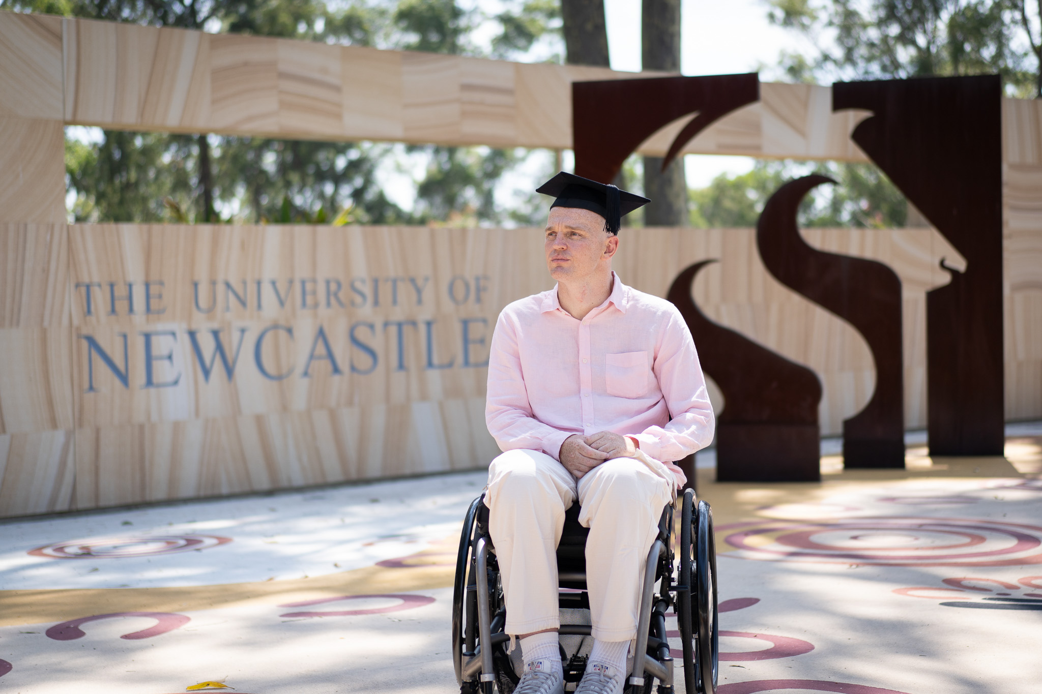 Alex McKinnon in a graduation cap in front of the University of Newcastle sign