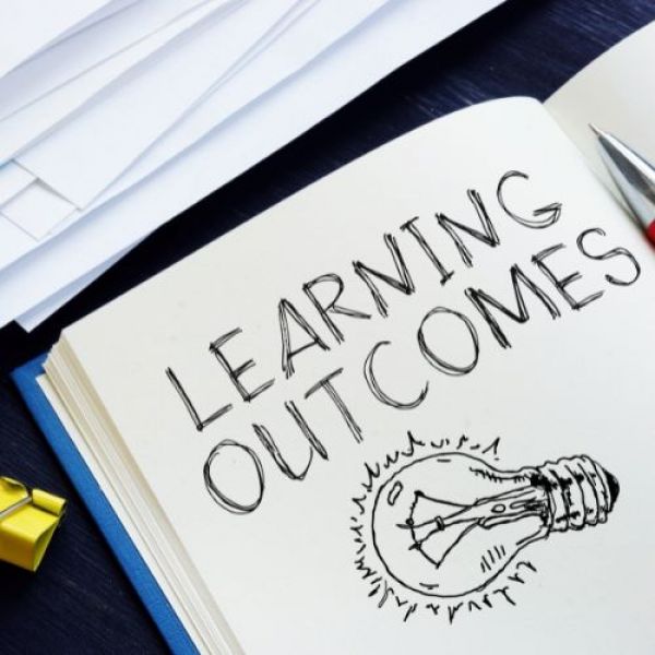 Learning Outcomes written in black pen with a black outline drawing of a lightbulb - Writing Weekly Learning Outcomes
