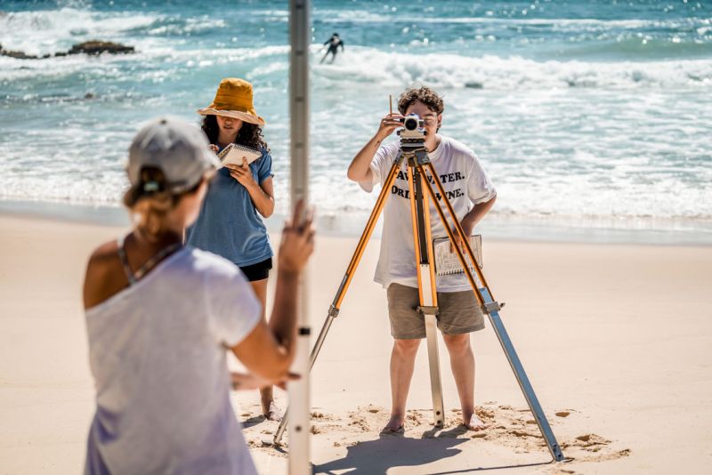 Students use surveying equipment on the beach