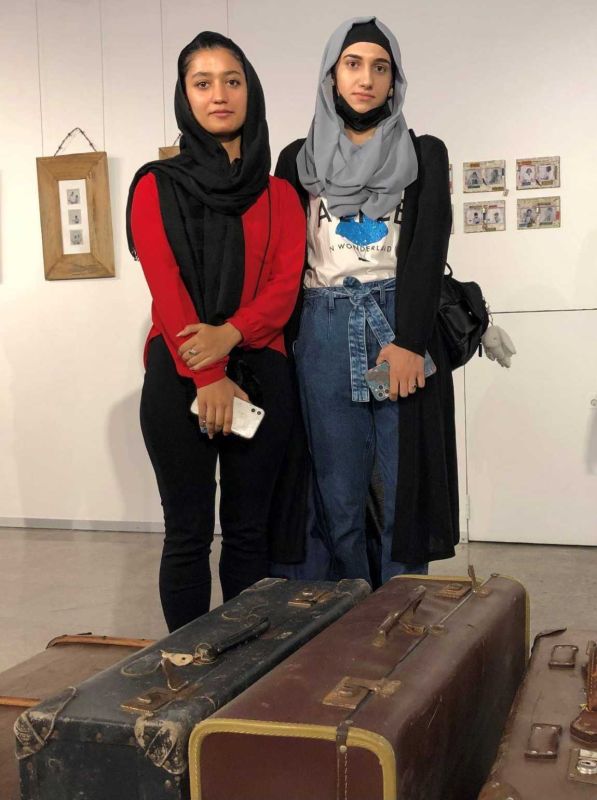 Two young women wearing headscarf old suitcases in foreground