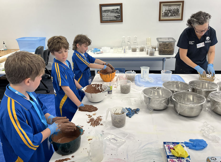 SMART Team Member Sonia stands at a table with three program participants, wearing gloves and mixing eco-housing materials in plastic bowls