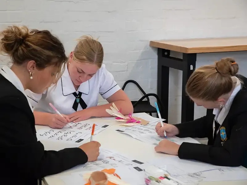 Three students work around a table with pens and paper.