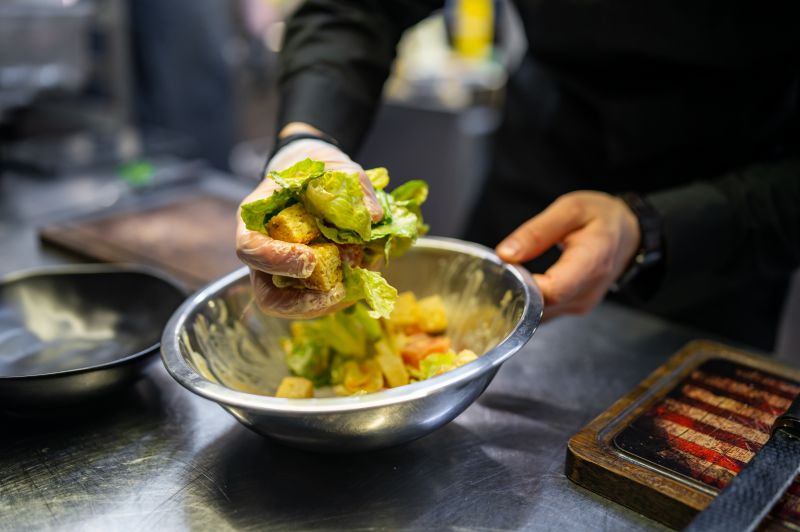 Someone tossing a bowl of ceasar salad with their hands