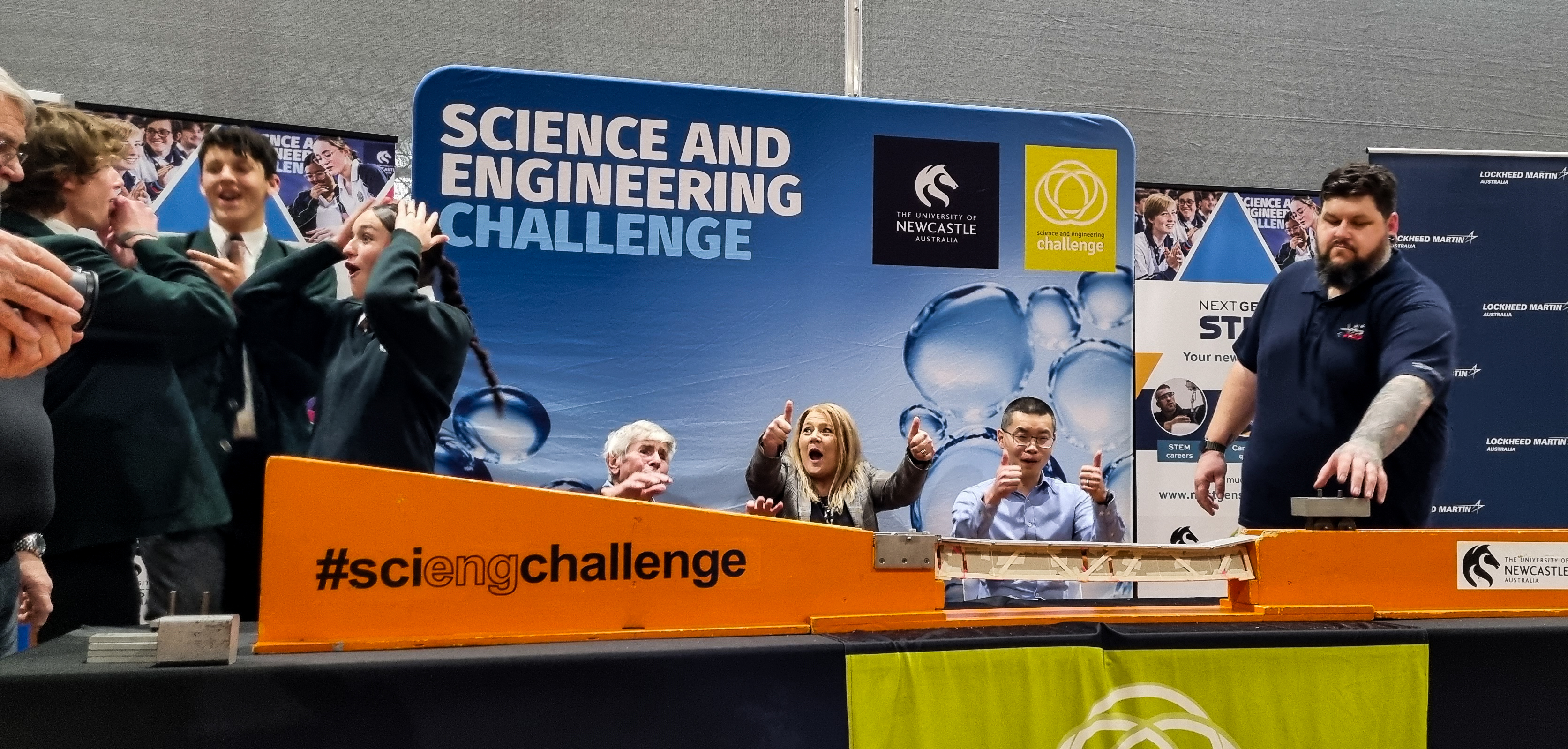 Students cheer at the State Finals bridge challenge School kids cheer as they pass the bridge building challenge. There are three judges in the back also cheering, as well as an adjudicator.