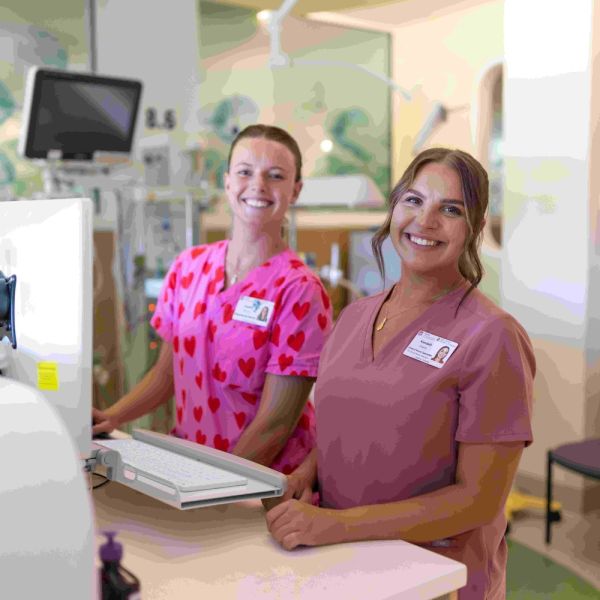 Two females in nursing scrubs smiling and sitting at a computer desk