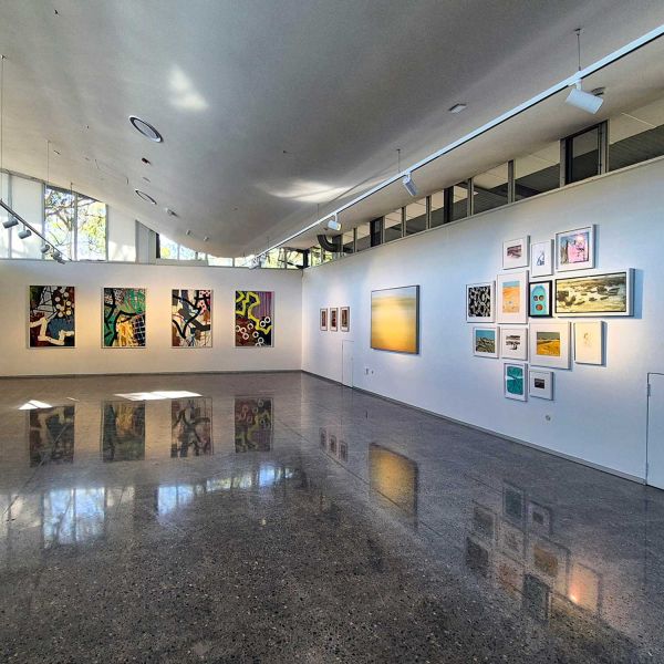Image showing a collection of artworks, spread across a corner section inside the University Gallery.. Community Support for the Arts.