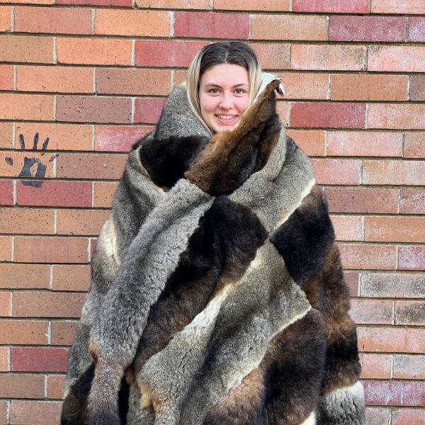 High school students standing in front of a brick wall wrapped warmly in a possum skin cloak looking excited and happy