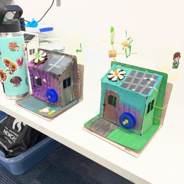 Two brightly-coloured, decorated, eco-houses sit on a table. Young innovators explore sustainable housing through SMART eco-house program.