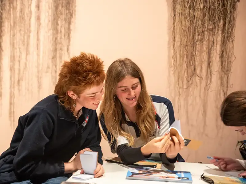 Two students sitting together looking at a small notebook.