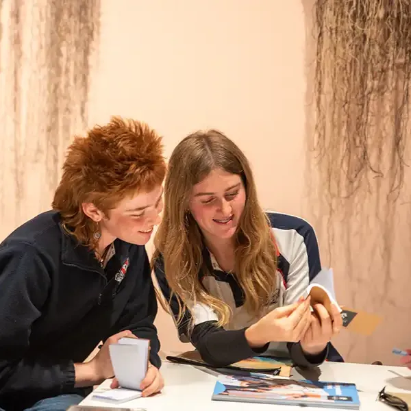 Two students sitting together looking at a small notebook.
