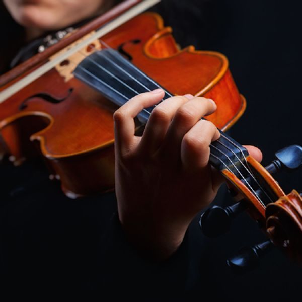 A close-up of a violin being played, showing a musician’s hand on the fingerboard and bow across the strings against a dark background.